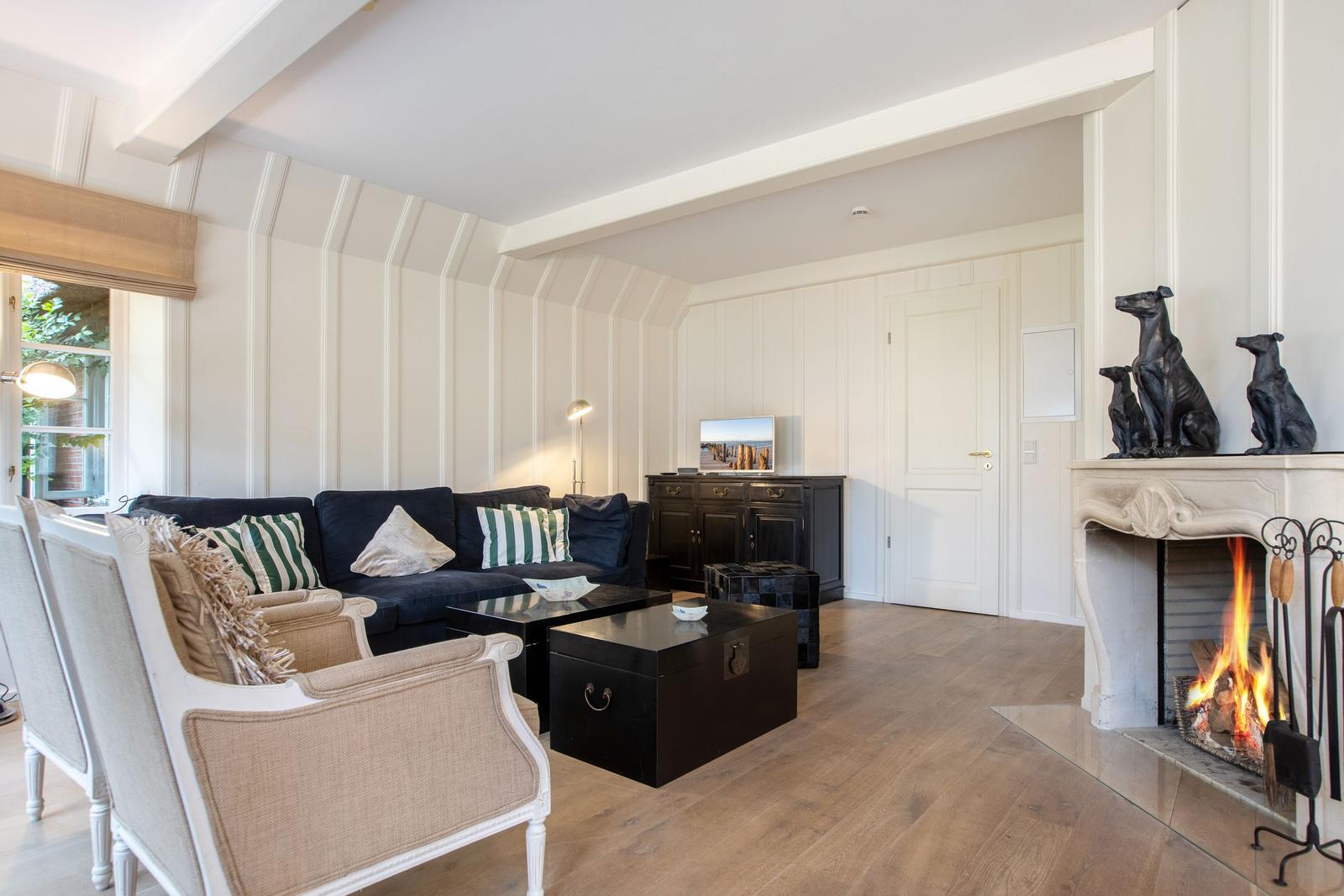 Living room with fireplace, sofa and chairs. Wooden floor and white walls.