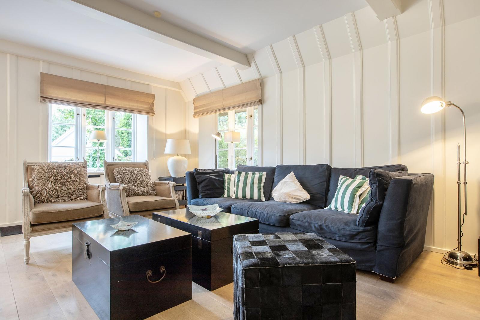 Living room with sofa, two armchairs, tables, and windows.