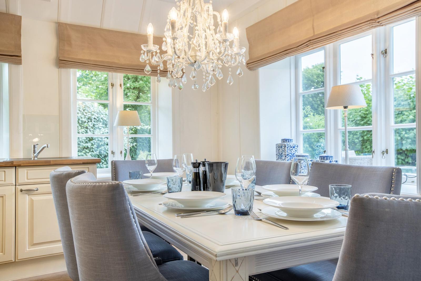 Dining room with table, chairs, and chandelier. Windows overlooking garden.