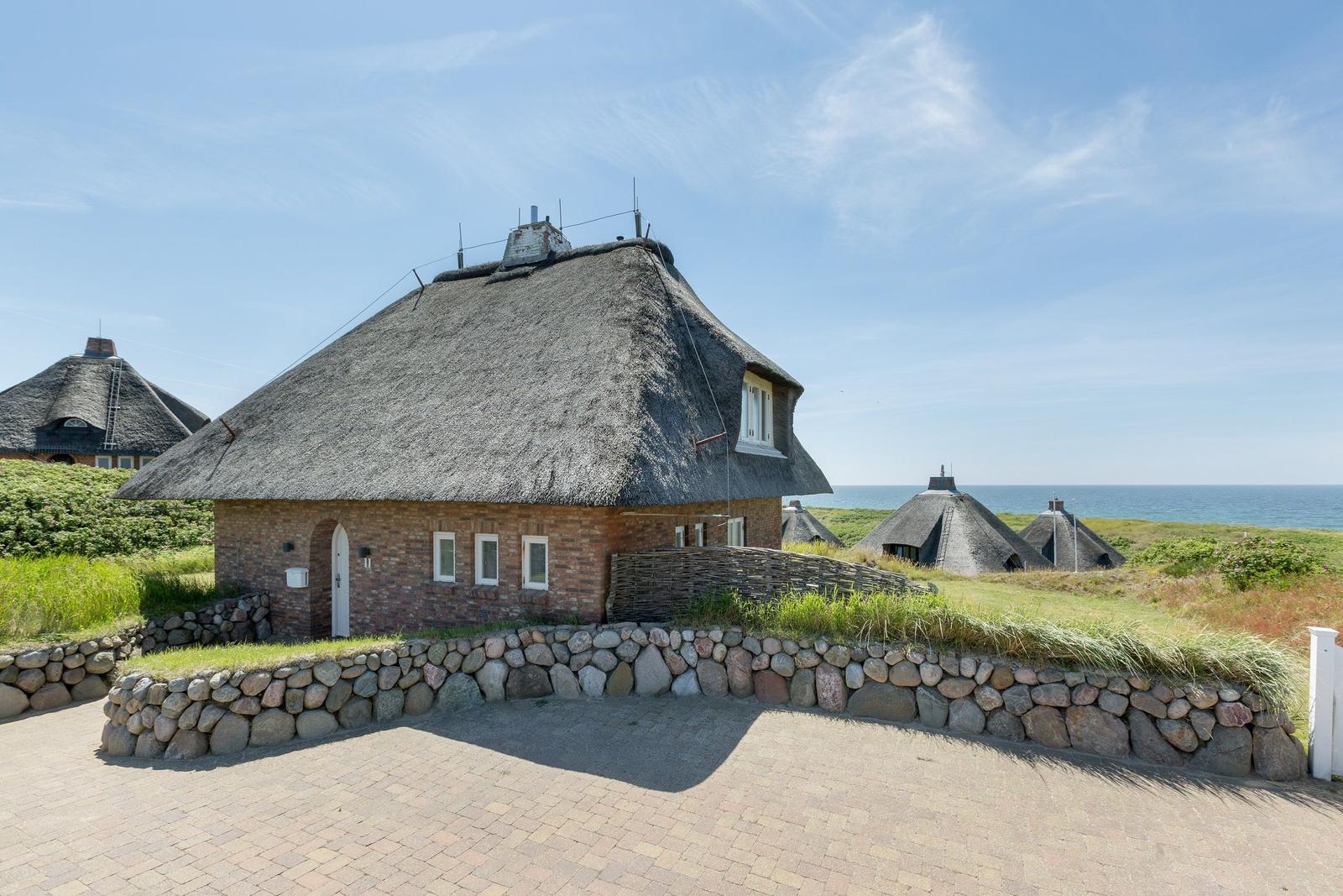 Haus mit Strohdach, Steinmauer und Blick aufs Meer.