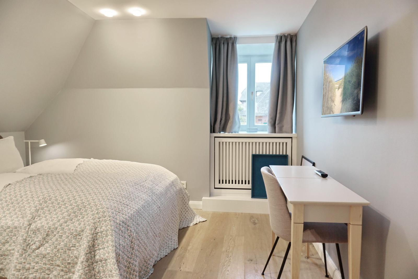 Schlafzimmer mit Bett, Schreibtisch und Fernseher an der Wand.