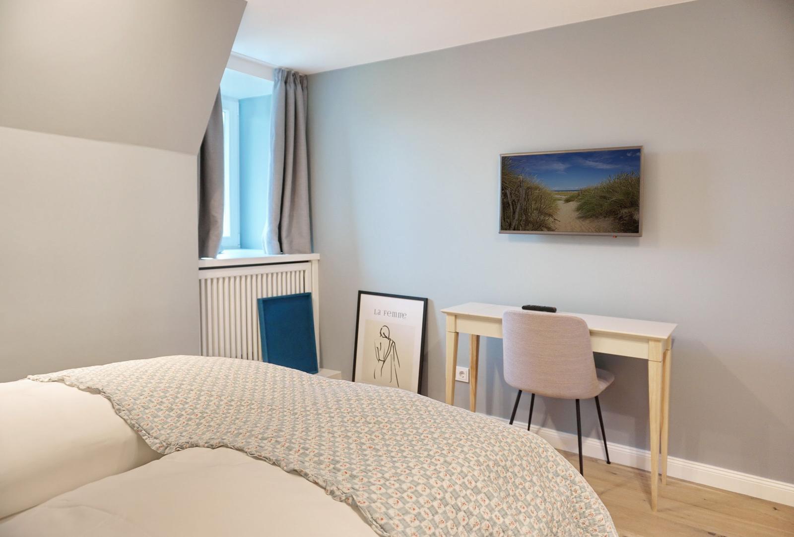 Schlafzimmer mit Bett, Schreibtisch und Wandbild.