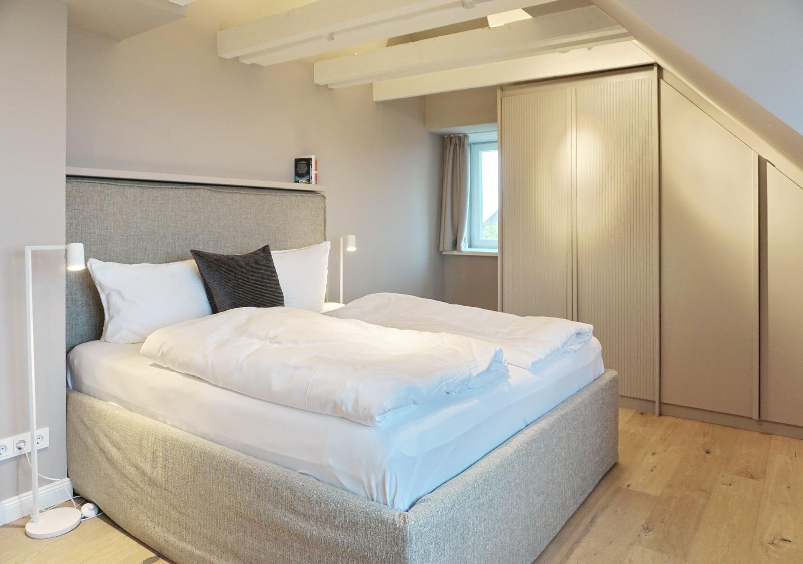 Schlafzimmer mit Bett, Kleiderschrank und Fenster.