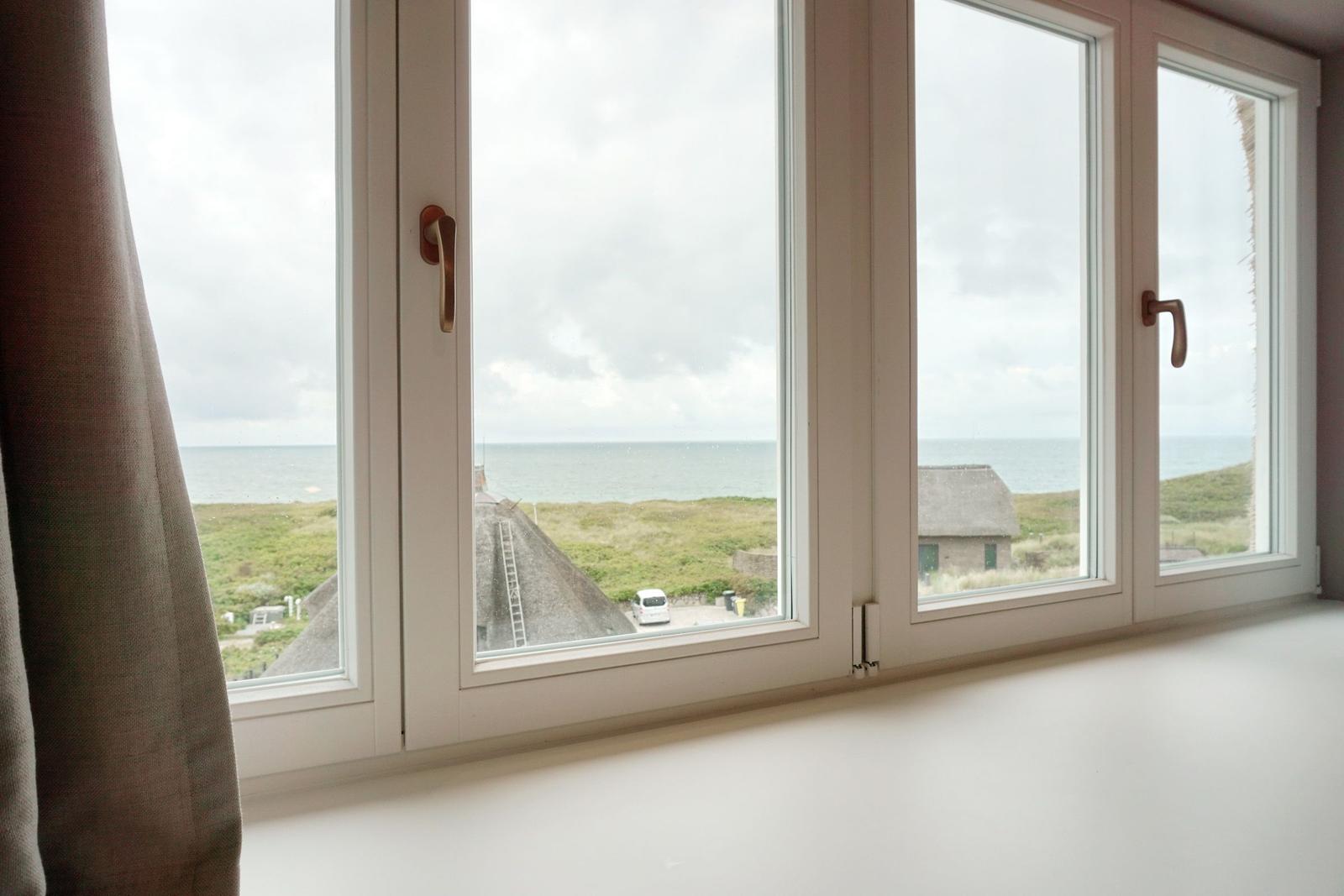 Durch das Fenster ist das Meer und eine grüne Landschaft mit Häusern sichtbar.