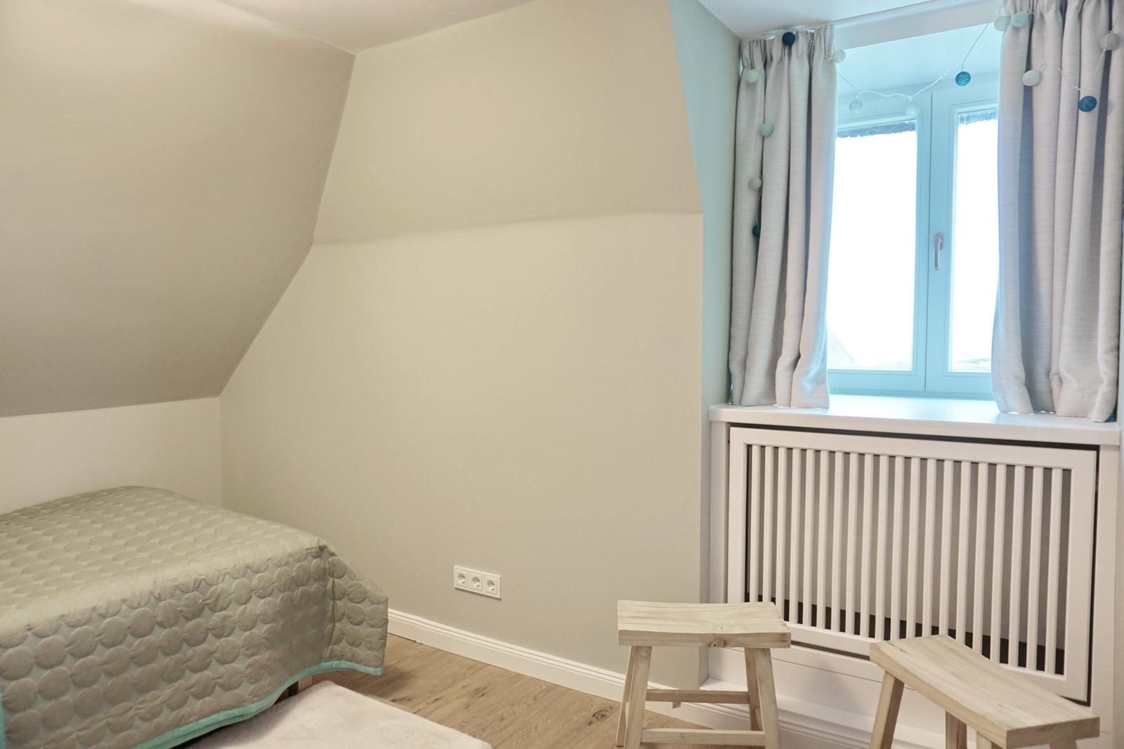 Zimmer mit Bett, Fenster und Holzmöbeln. Dachschrägen und weiße Wände.