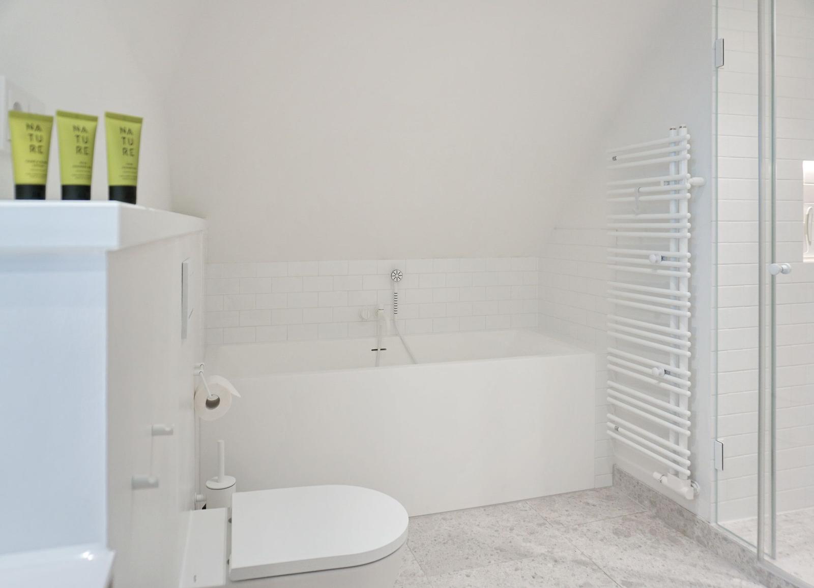 Bad mit Badewanne, Toilette und Dusche. Drei grüne Flaschen auf dem Waschtisch.