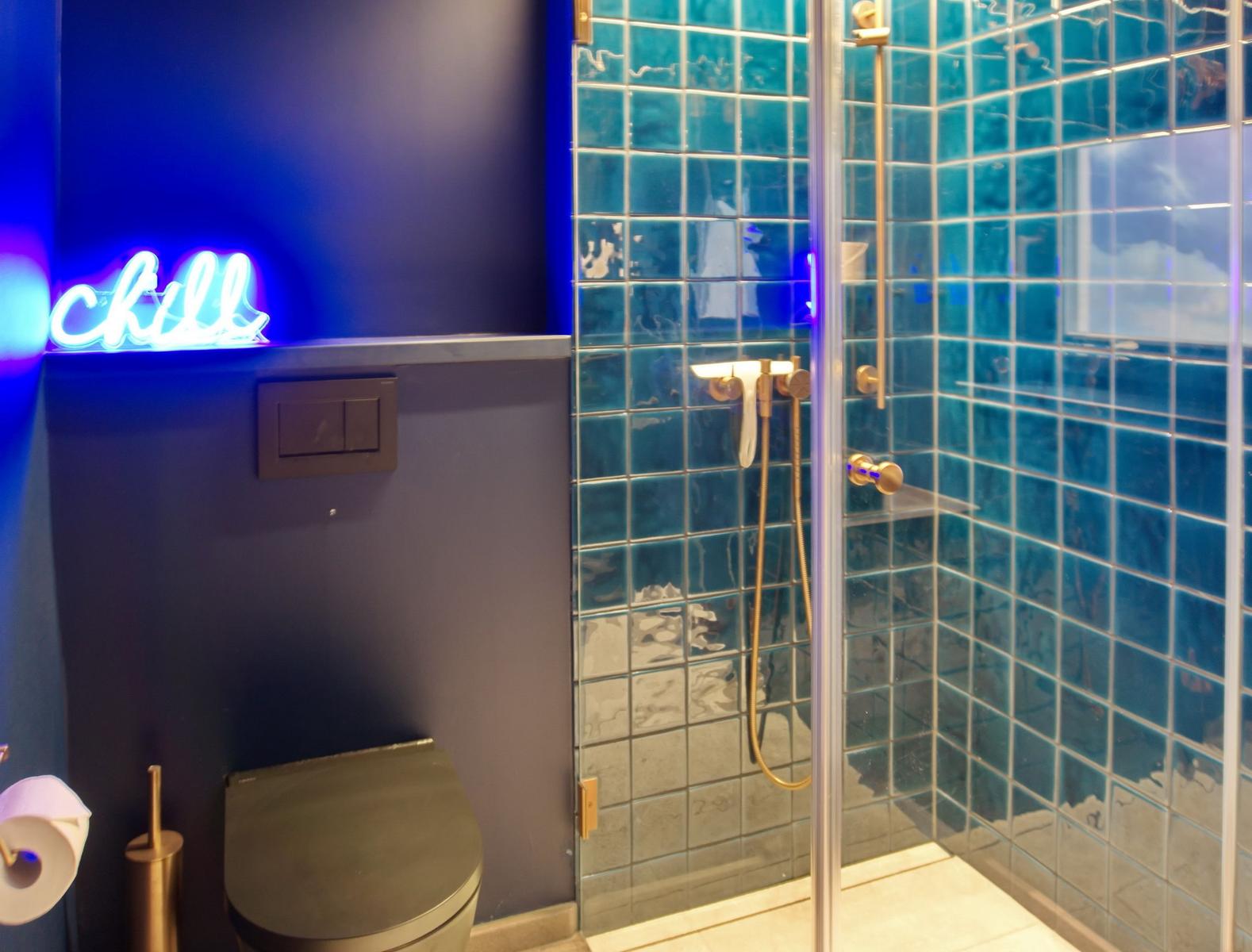 Badezimmer mit Dusche, Toilette und Neonlicht.