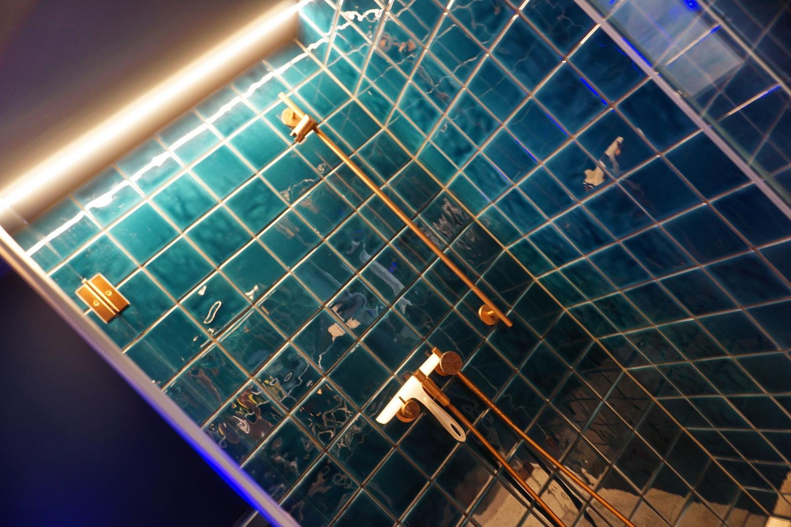 Duschbereich mit blauen Fliesen und goldenen Armaturen