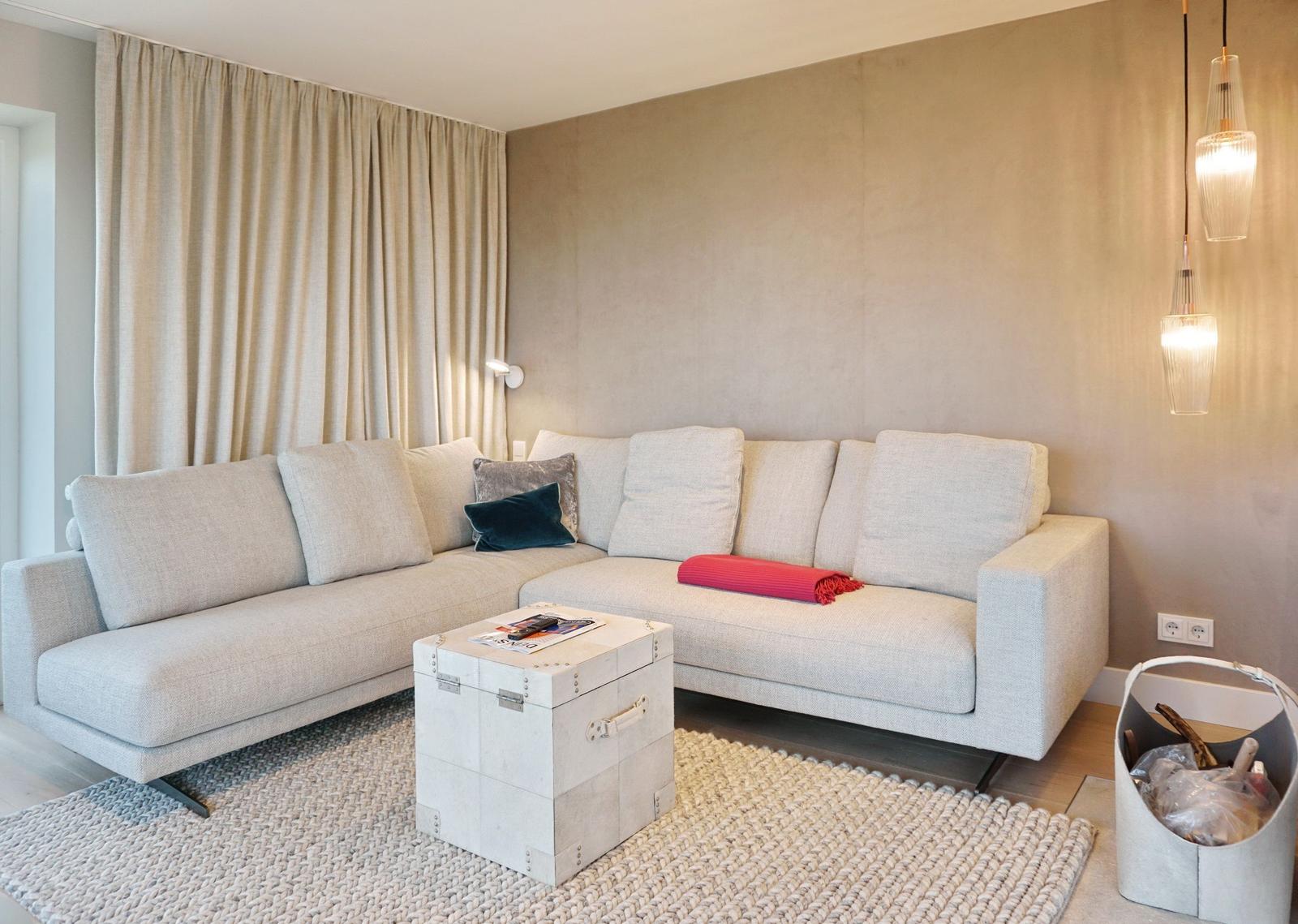 Ein Wohnzimmer mit einem hellen Ecksofa, einem Koffer-Tisch und hängenden Lampen.