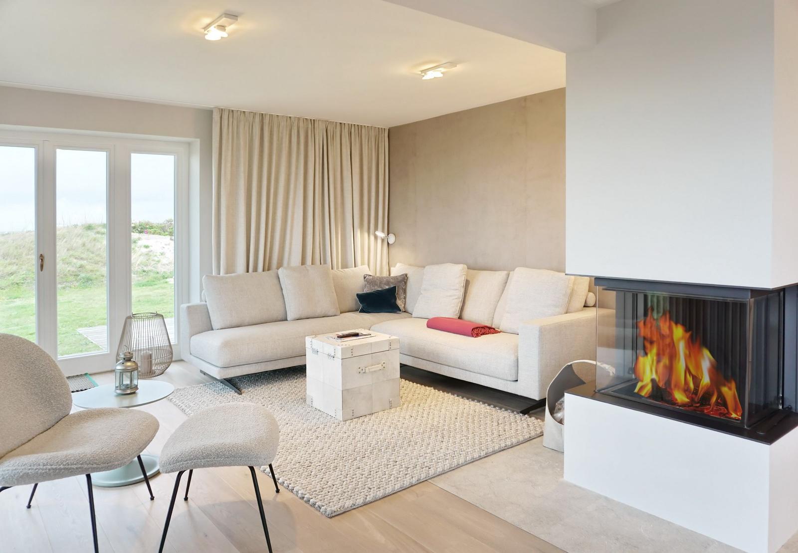 Wohnzimmer mit Sofa, Kamin und Blick auf Grünfläche.