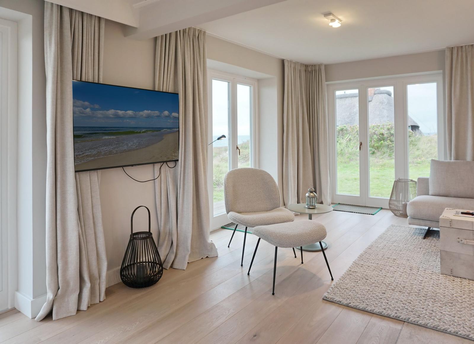 Wohnzimmer mit Fernseher, Sitzgelegenheiten und Blick auf Grünflächen.