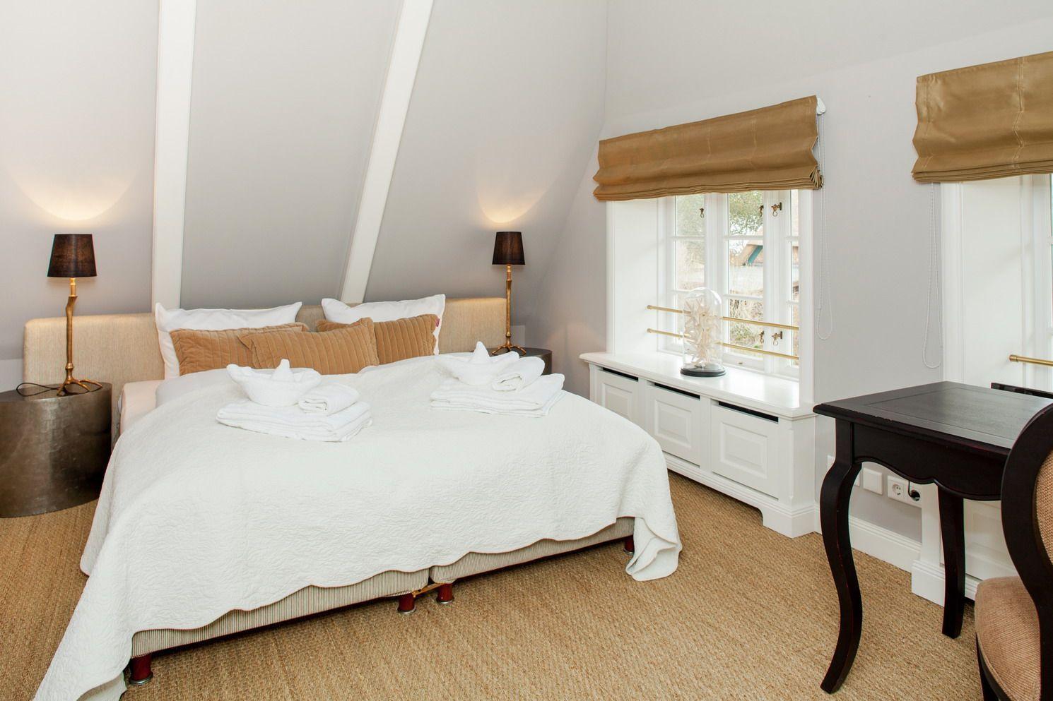 Schlafzimmer mit Doppelbett, zwei Nachttischen und Schreibtisch. Fenster mit Rollladen und Wandlampe.