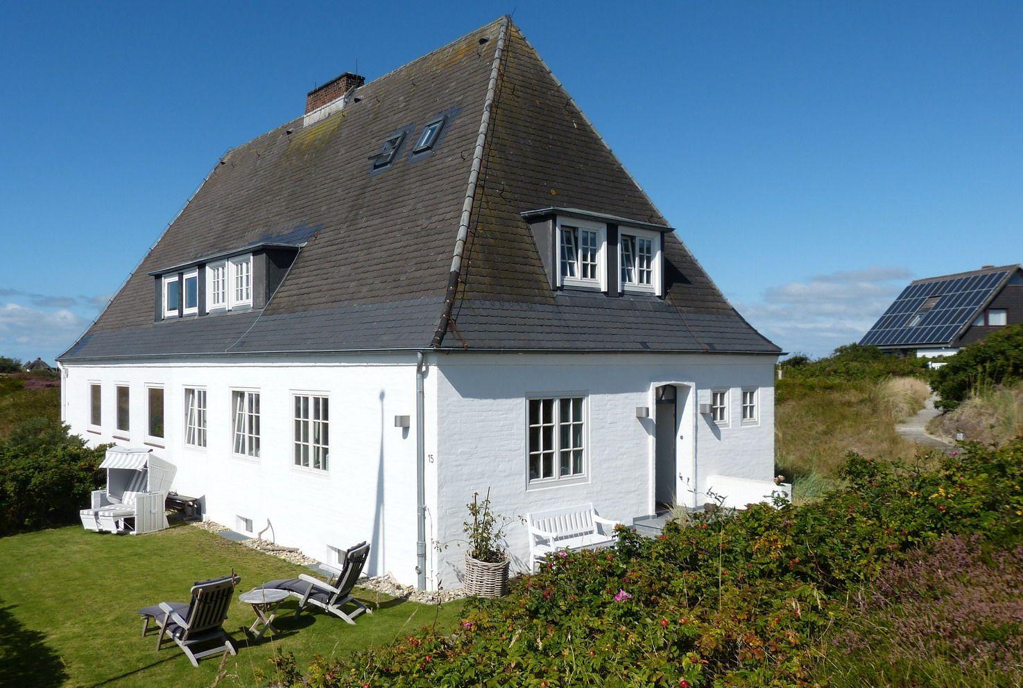 White house with gray roof, garden with lounge chairs and flower beds.
