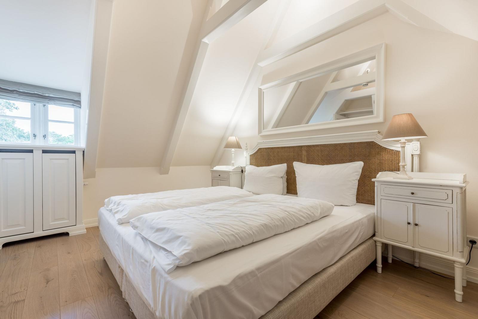 Schlafzimmer mit Doppelbett, zwei Nachttischen und Spiegel an der Wand.