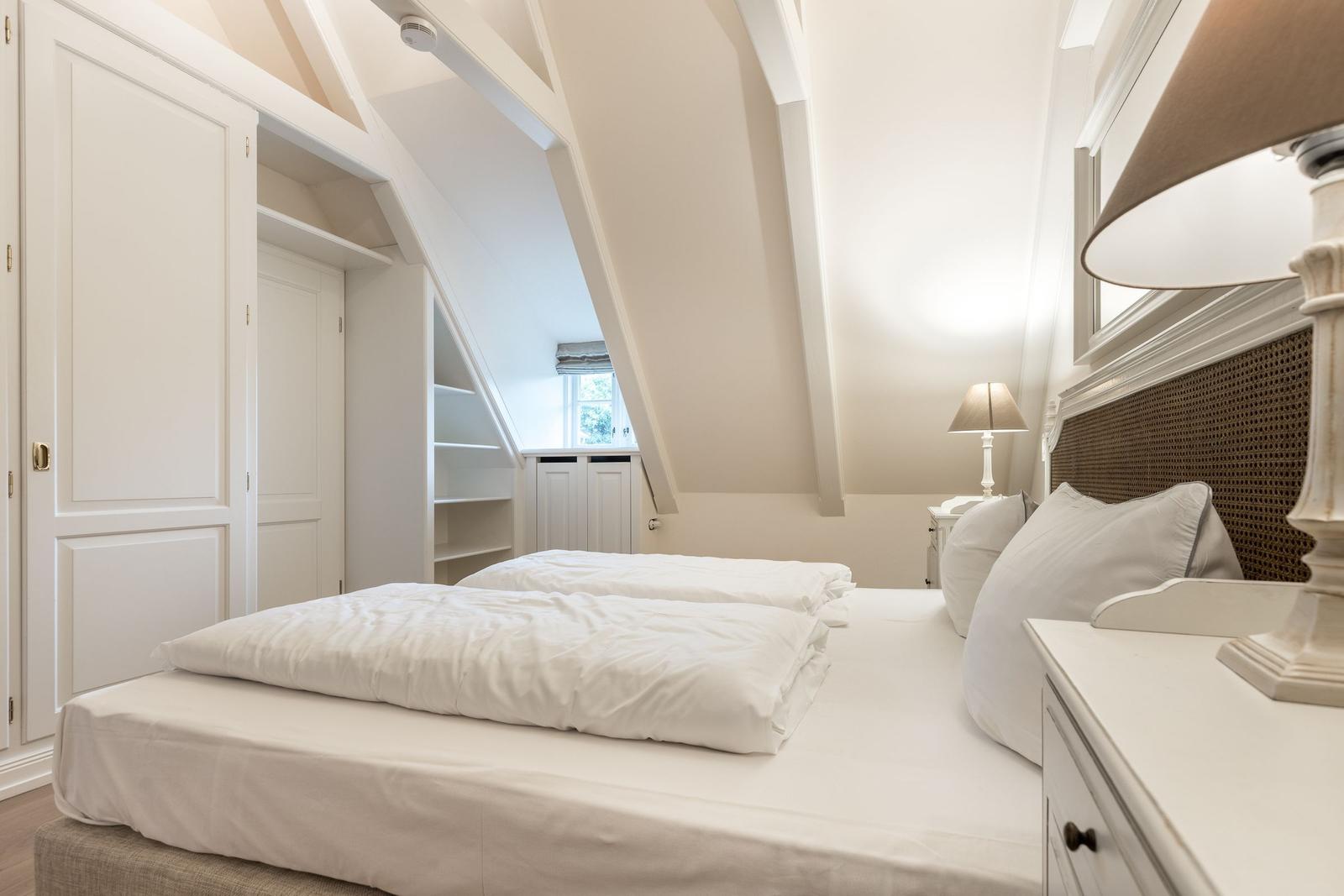 Schlafzimmer mit Doppelbett, Kleiderschrank und Dachschränken.
