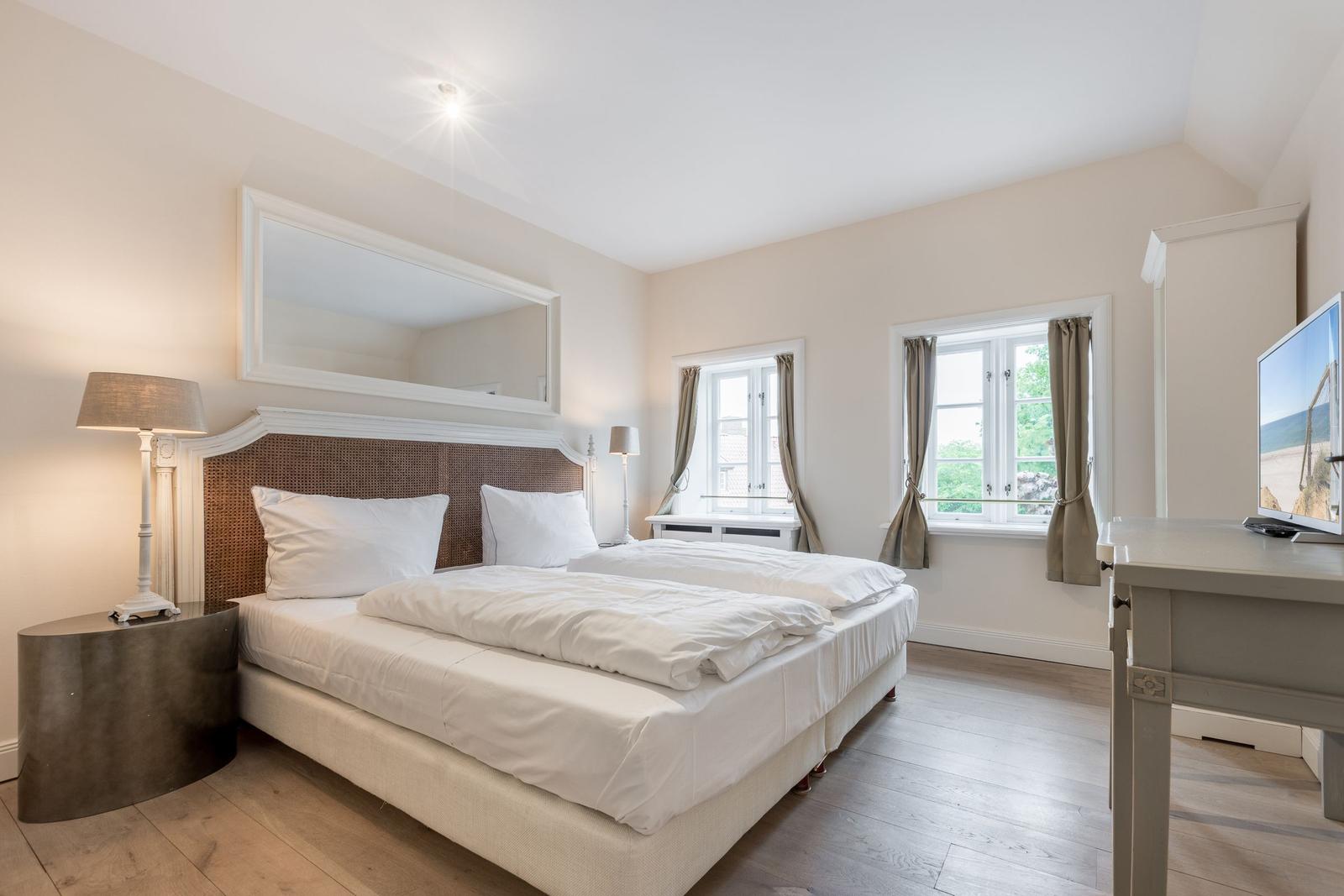 Schlafzimmer mit Doppelbett, Fenstern und Fernseher.