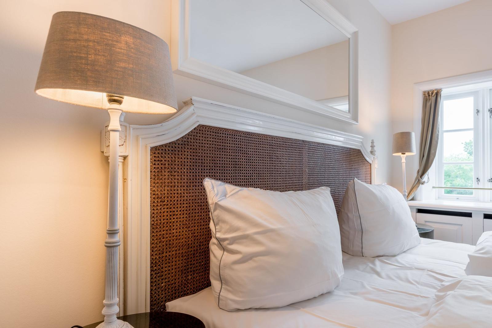 Schlafzimmer mit Bett, Kopfteil und Stehlampe. Fenster mit Vorhang.