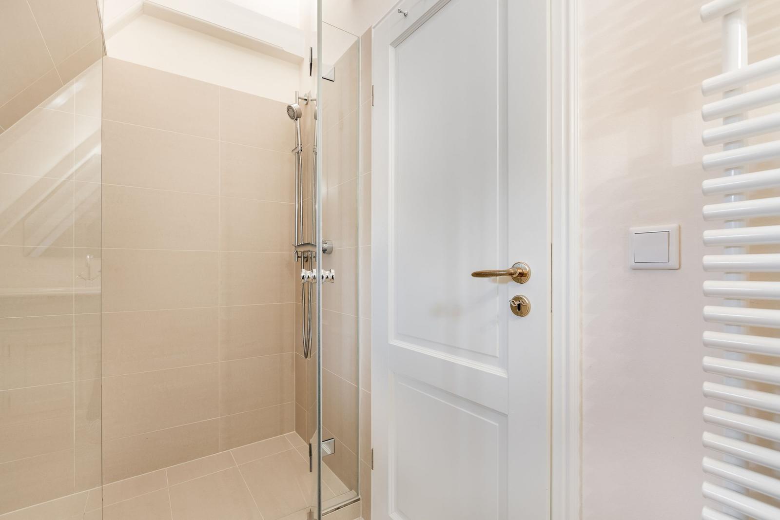 Dusche mit Glaswand, weiße Tür und Heizkörper