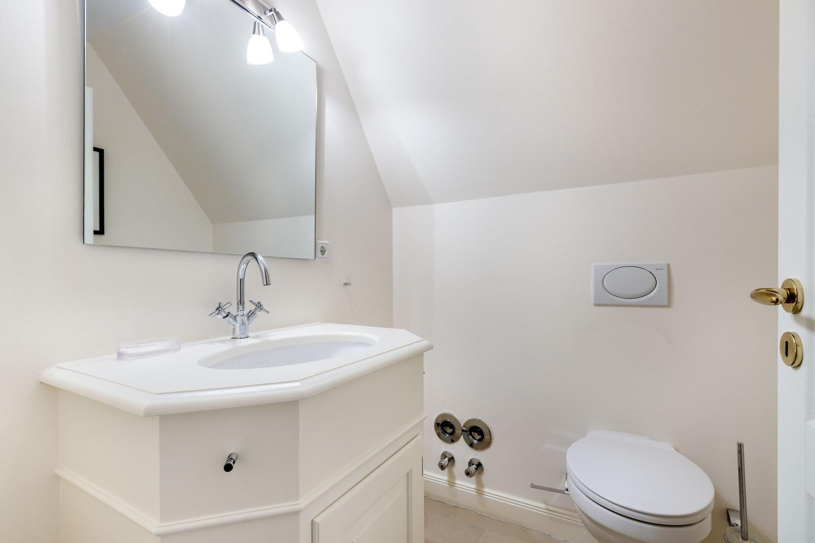 Badezimmer mit Waschbecken, Spiegel und Toilette unter Dachschrägen.