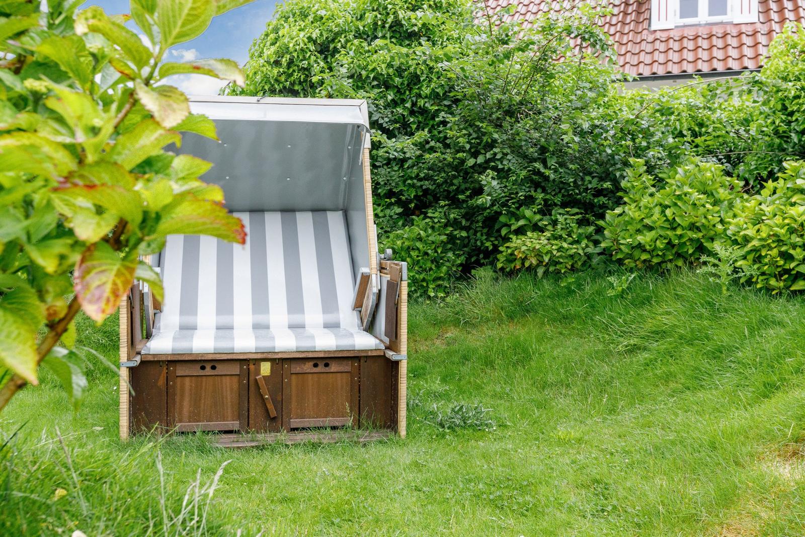 Hochbeet mit Streifenbezug im Garten. Hintergrund: grüne Hecke und Haus.