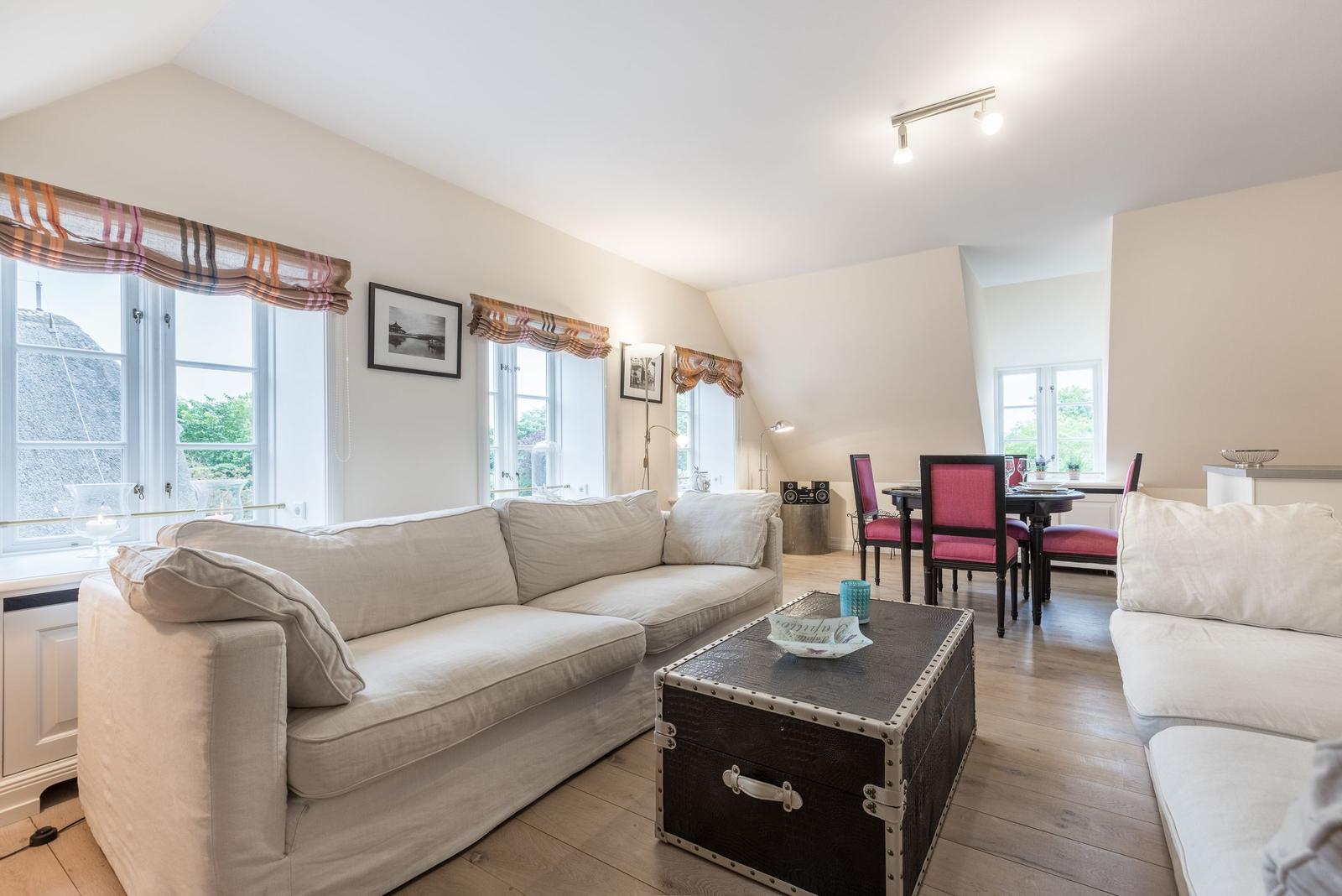 Wohn- und Essbereich mit Sofa, Tisch und Stühlen. Holzboden und große Fenster.