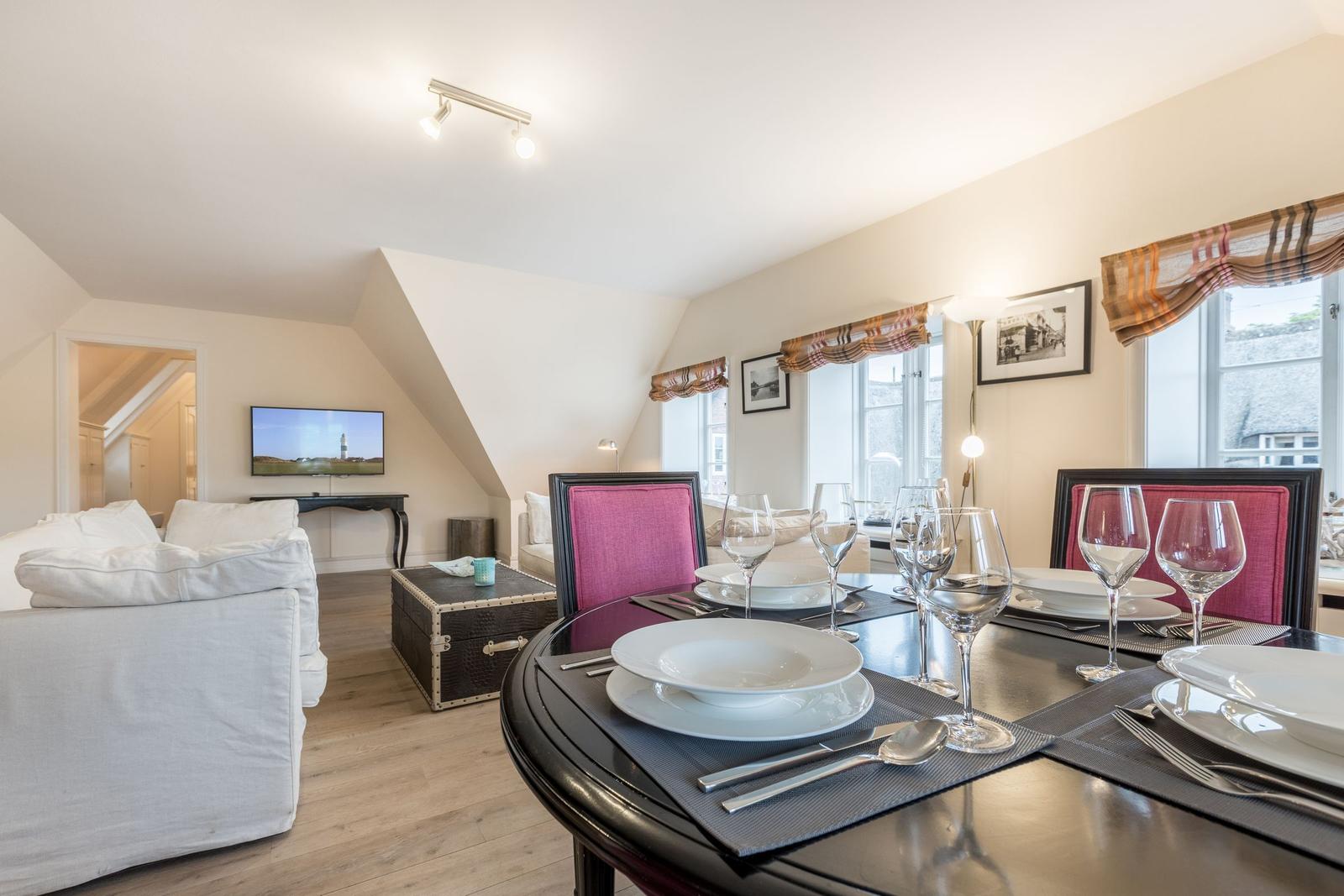 Esszimmer mit runder Tisch und pinken Stühlen. Wohnbereich mit Sofa und Fernseher.