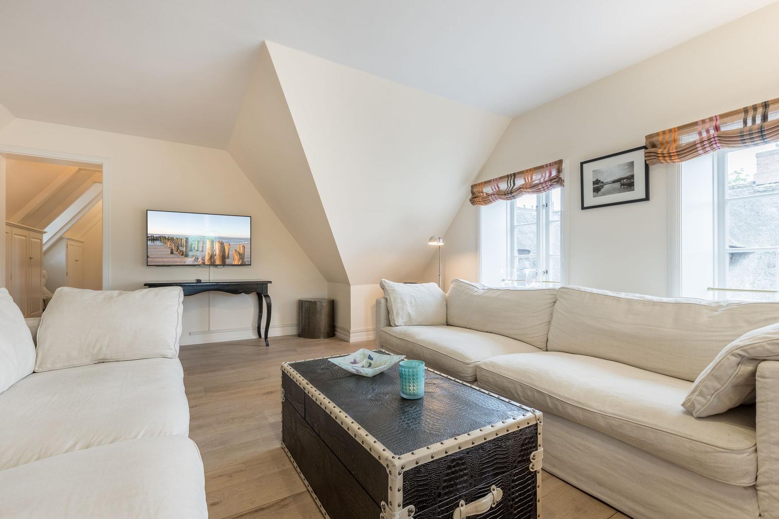 Wohnzimmer mit Sofa, Couchtisch und Fernseher unter Dachschrägen