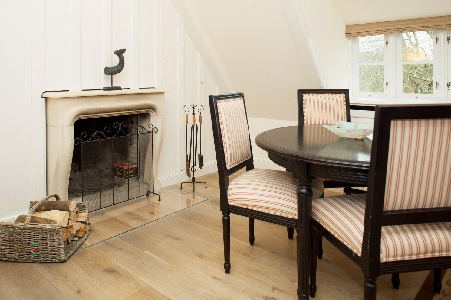 Dining room with round table, striped chairs, and fireplace with wood.