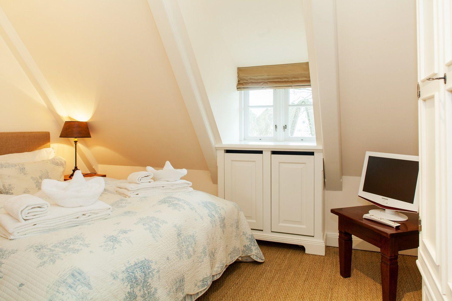Bedroom with bed, TV, and window under sloped ceiling.