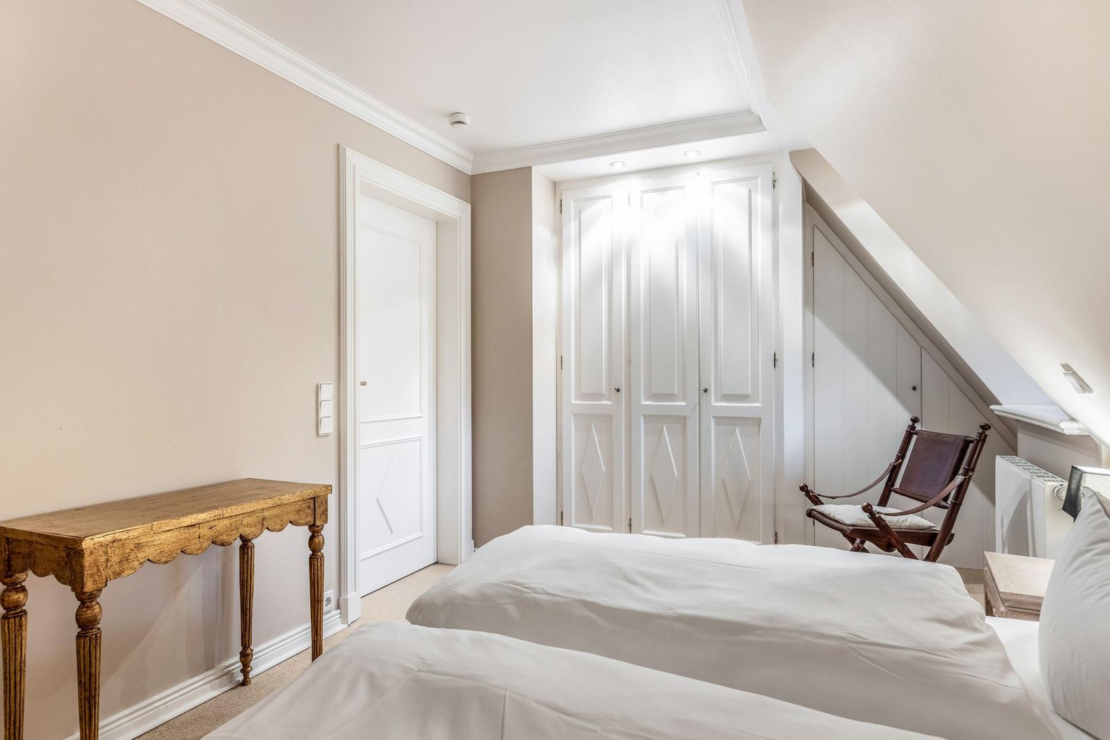 Schlafzimmer mit Bett, Schrank und Holzstuhl unter Dachschrägen.