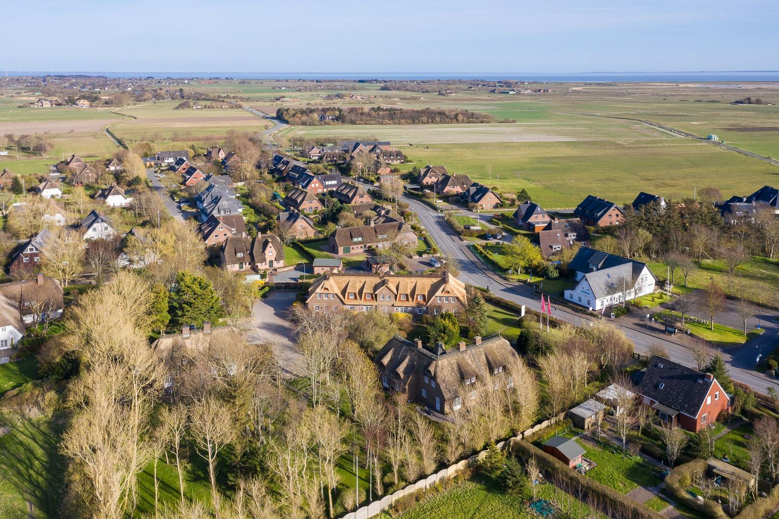 Dorf mit strohgedeckten Häusern und grünen Feldern am Meer