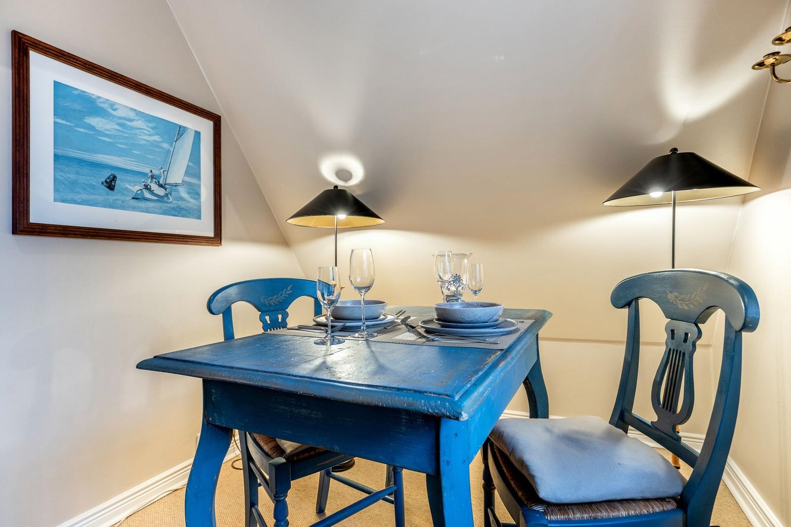 Blauer Esstisch mit zwei Stühlen, Bild an der Wand, zwei Lampen.