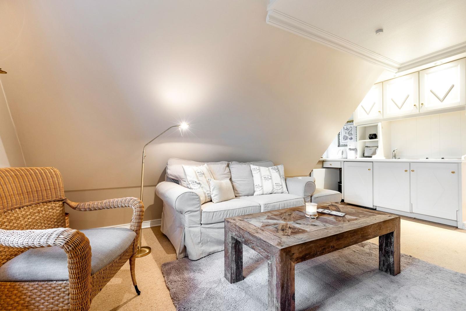 Wohnbereich mit Sofa, Sessel und Küchenzeile unter Dachschrägen.