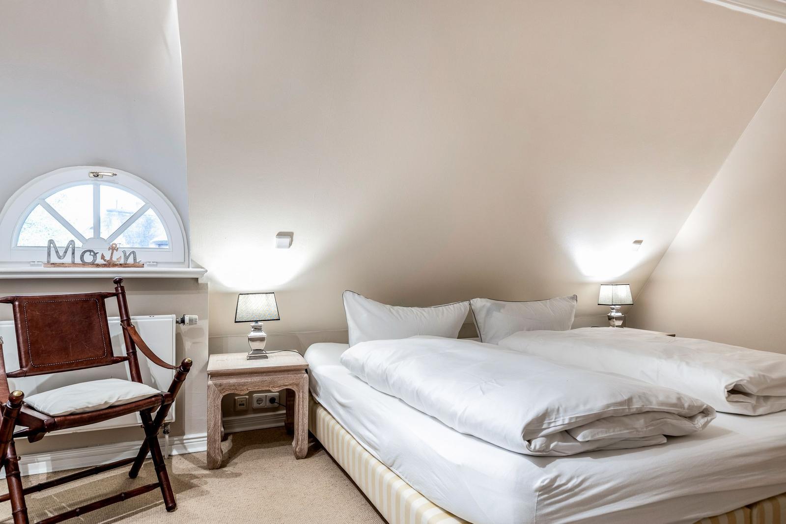 Schlafzimmer mit Doppelbett, Nachttisch und Stuhl unter schrägen Dachbodenwänden.