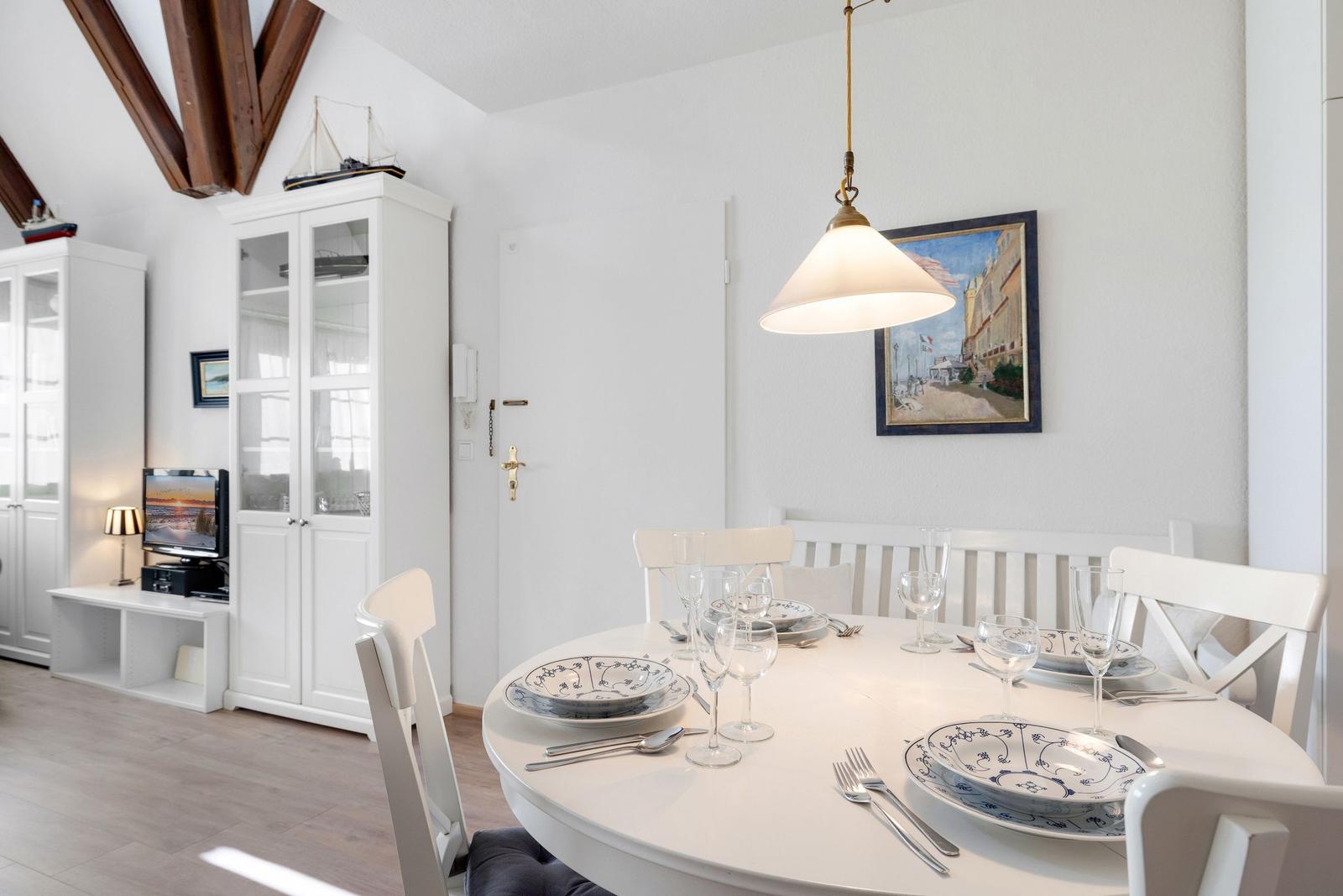 Rundtisch mit Platz für sechs Personen, weiße Stühle und Deckenbalken.