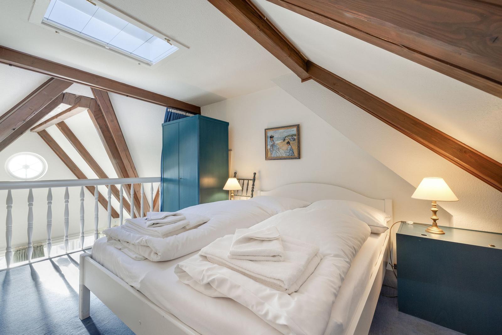 Schlafzimmer mit Dachschrägen, Bett, Kleiderschrank und Tischlampen.