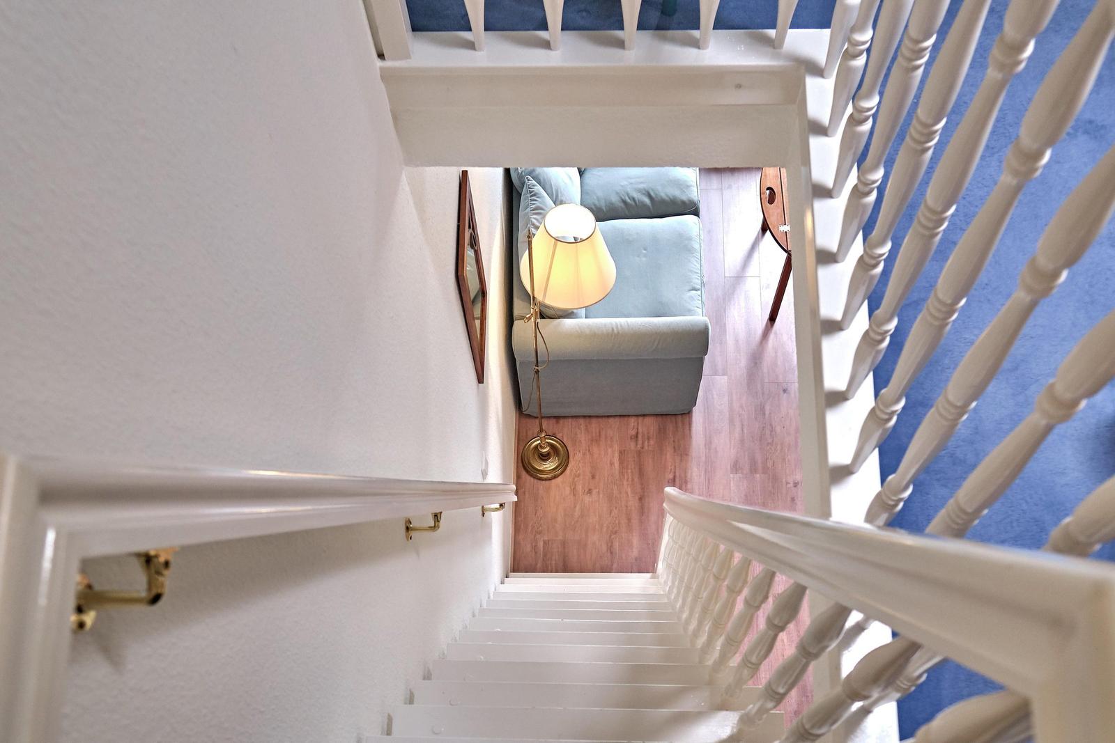 Treppenhaus mit Blick auf Wohnbereich mit Sofa und Stehlampe.