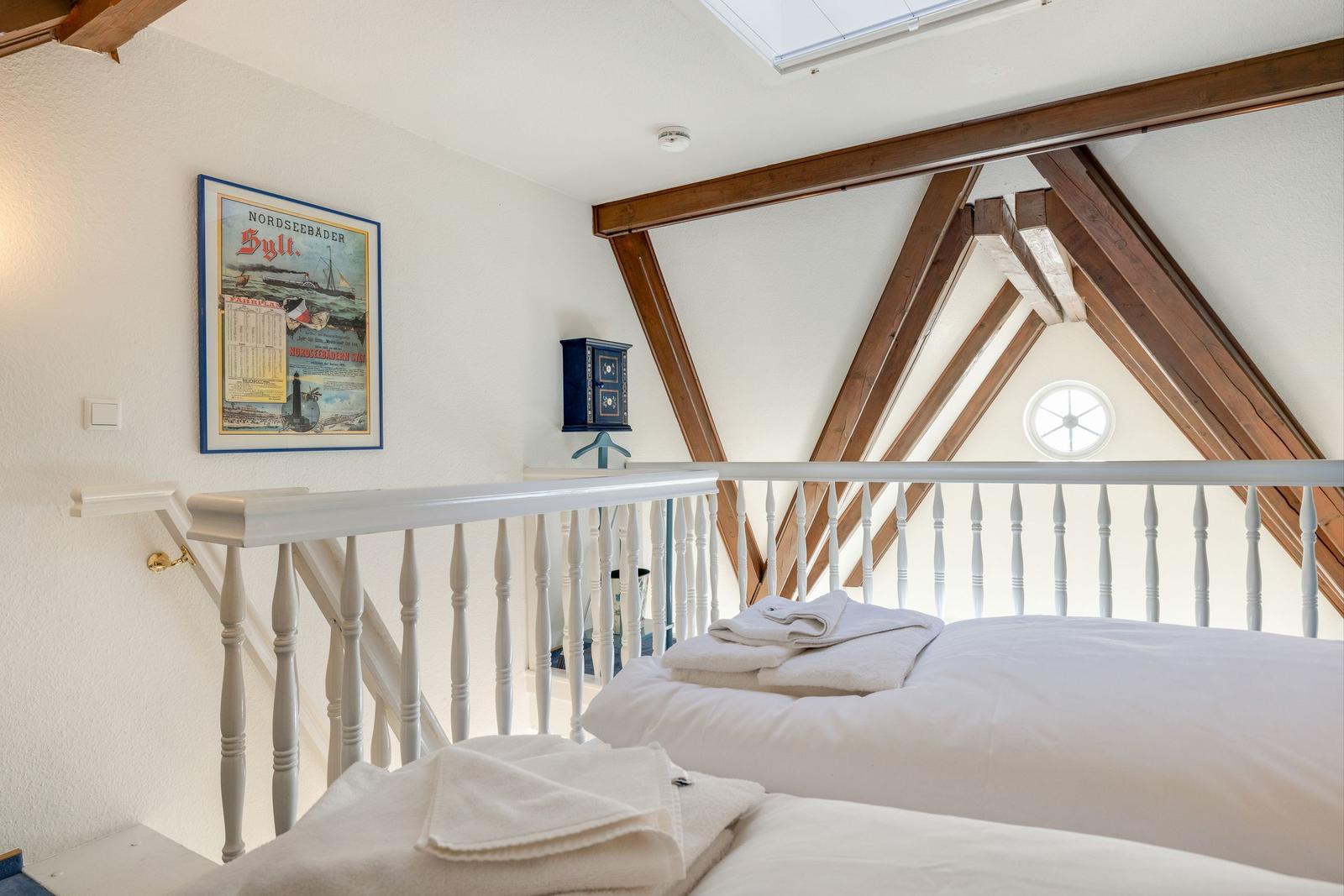 Schlafzimmer mit Dachschrägen, weißem Geländer und Poster an der Wand.