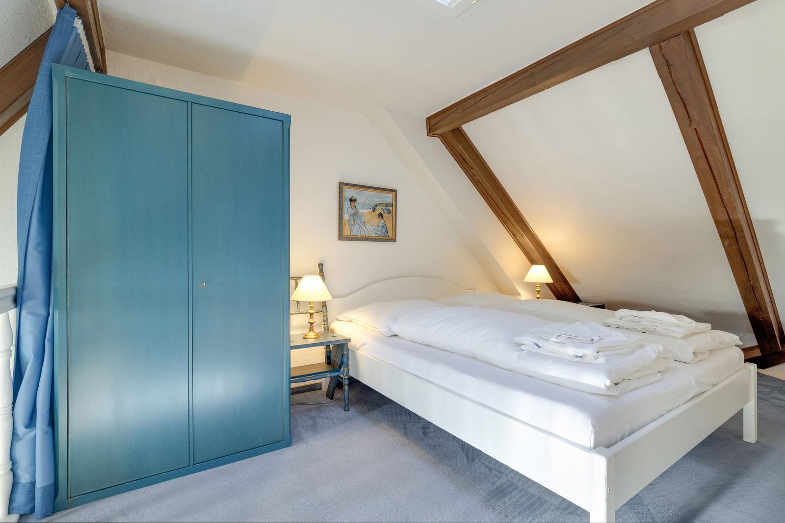 Schlafzimmer mit Doppelbett, blauem Schrank und Holzbalken an der Decke.