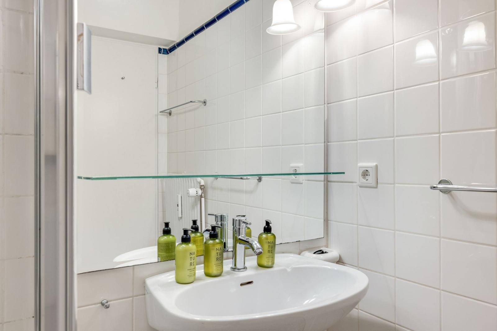 Badezimmer mit Waschbecken, Spiegel und grünen Flaschen.