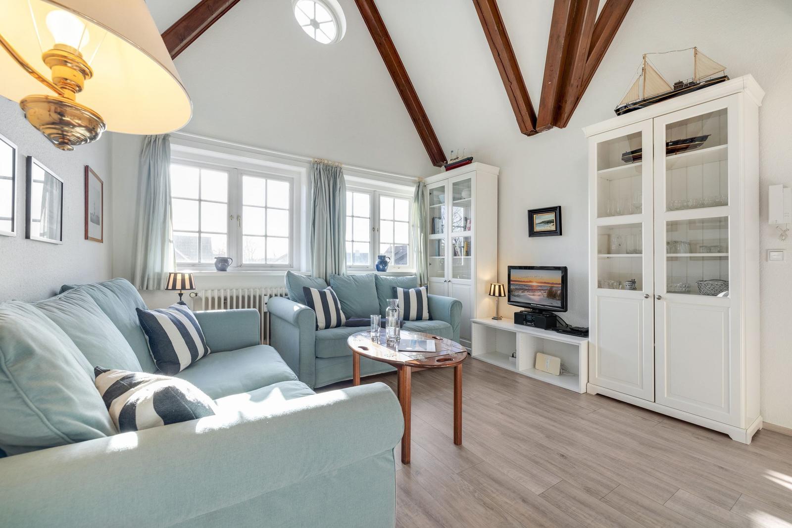 Wohnzimmer mit hellblauen Sofas, Holzboden und weißen Schränken unter hohem Dach.