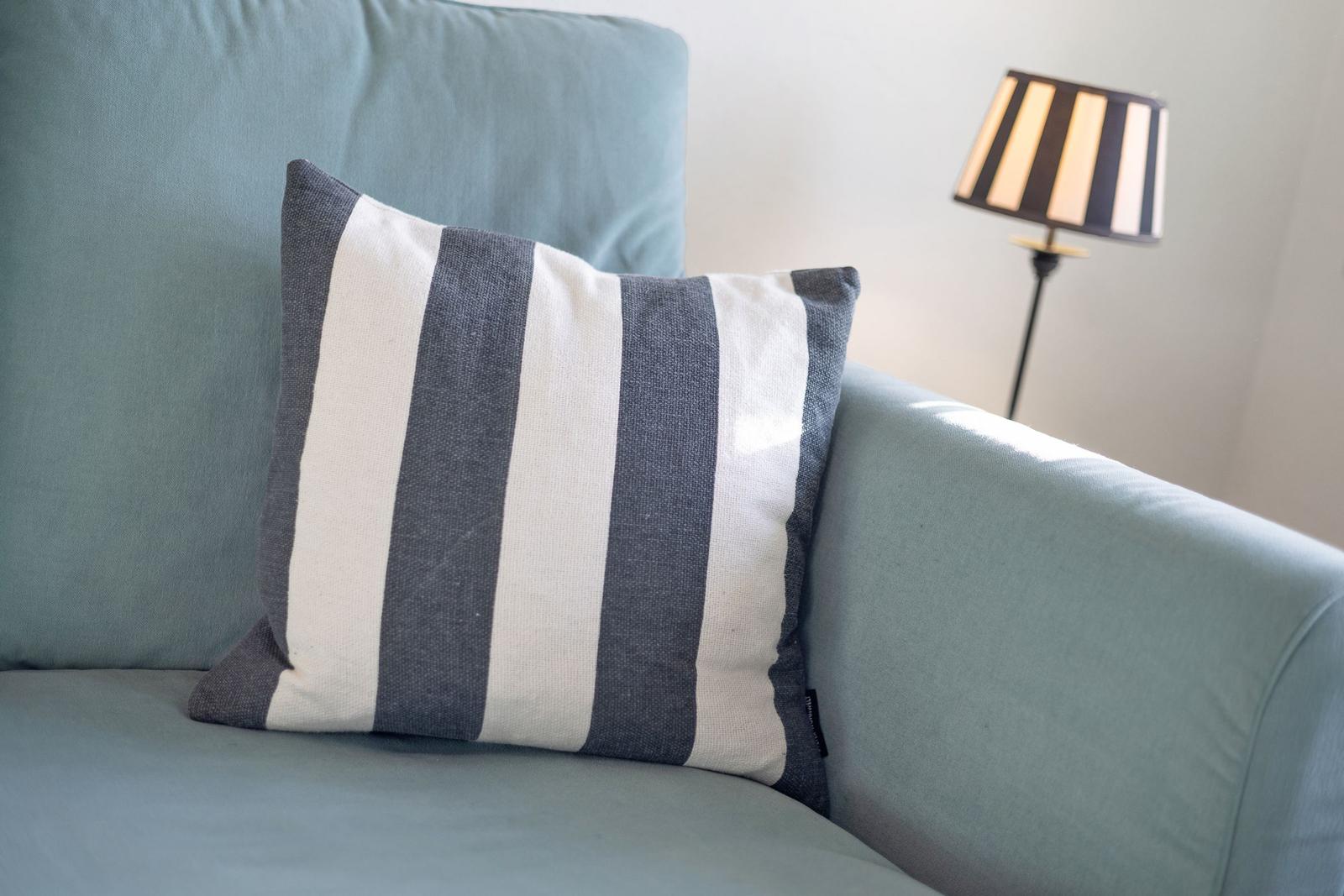 Ein Kissen mit Streifen liegt auf einem Sofa. Eine Stehlampe steht daneben.