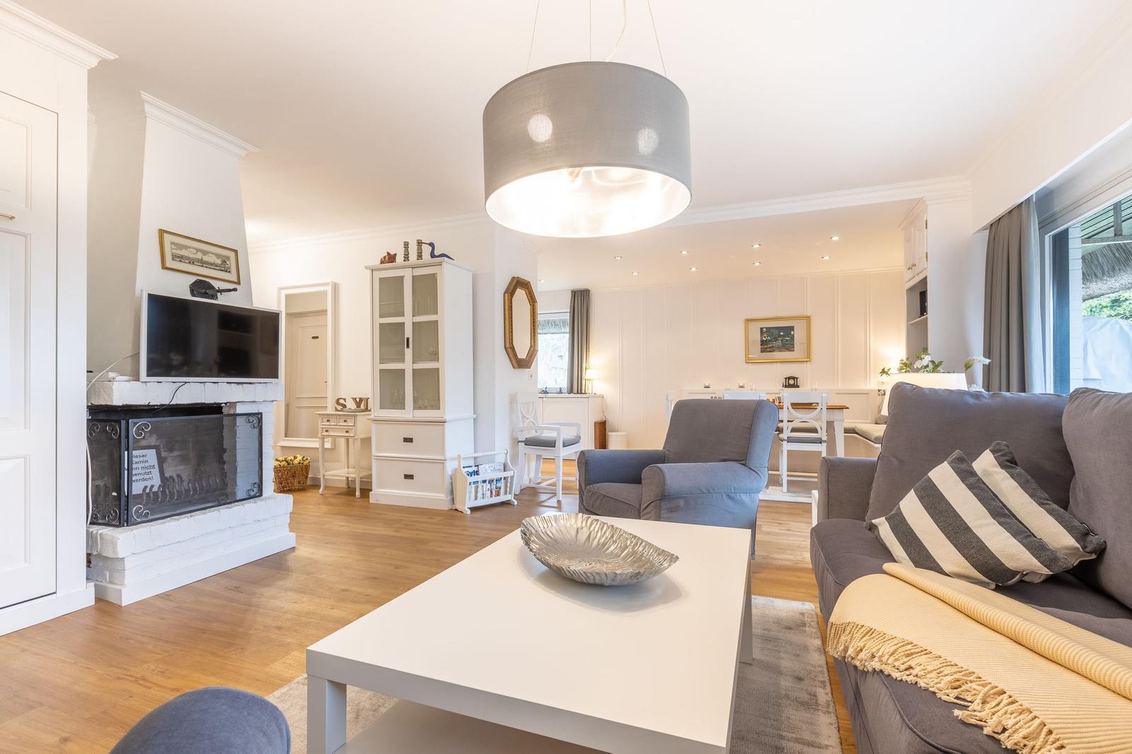 Wohnzimmer mit Sofa, Kamin und Esstisch im Hintergrund.