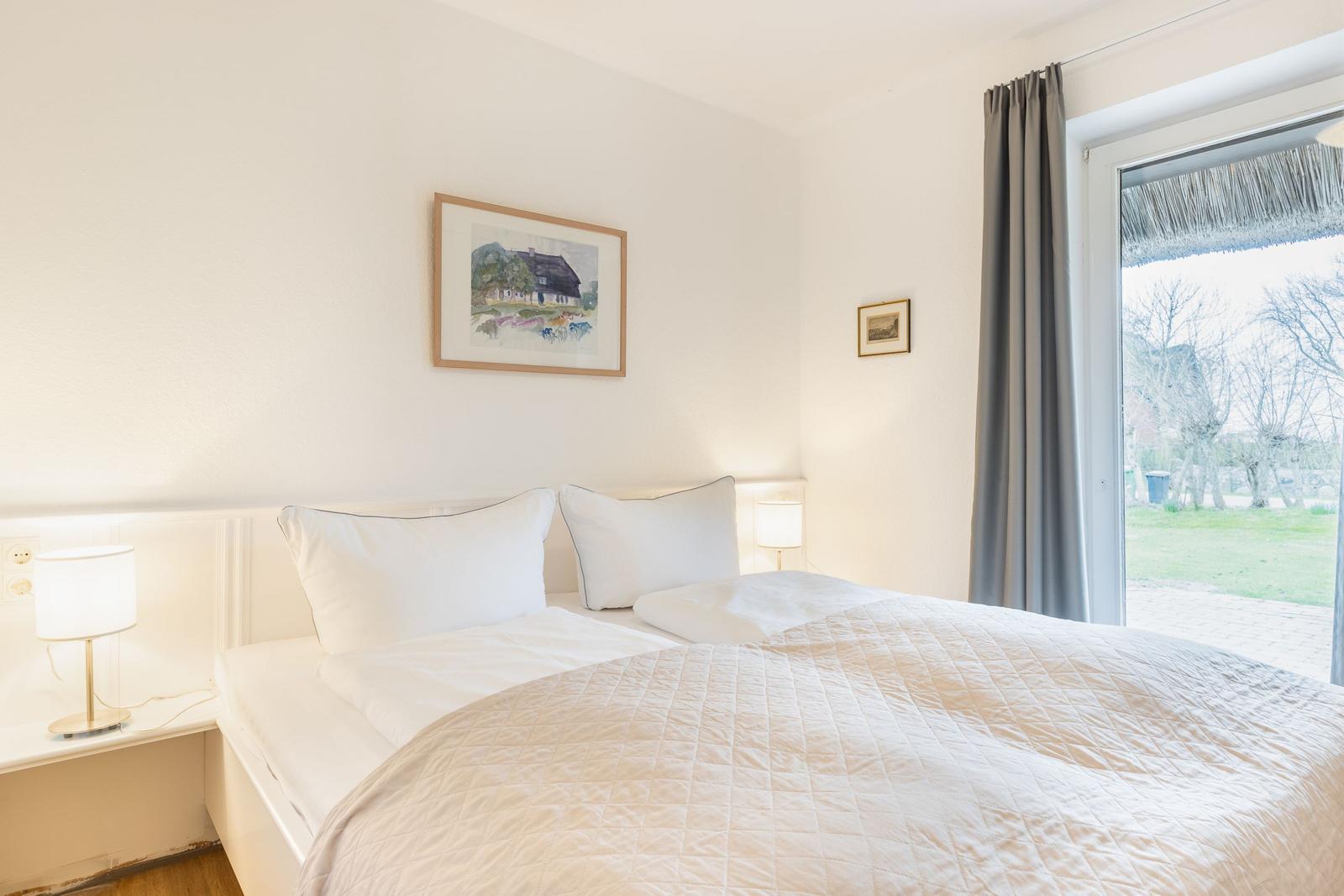 Schlafzimmer mit Bett, Lampen und Fensterblick auf Garten