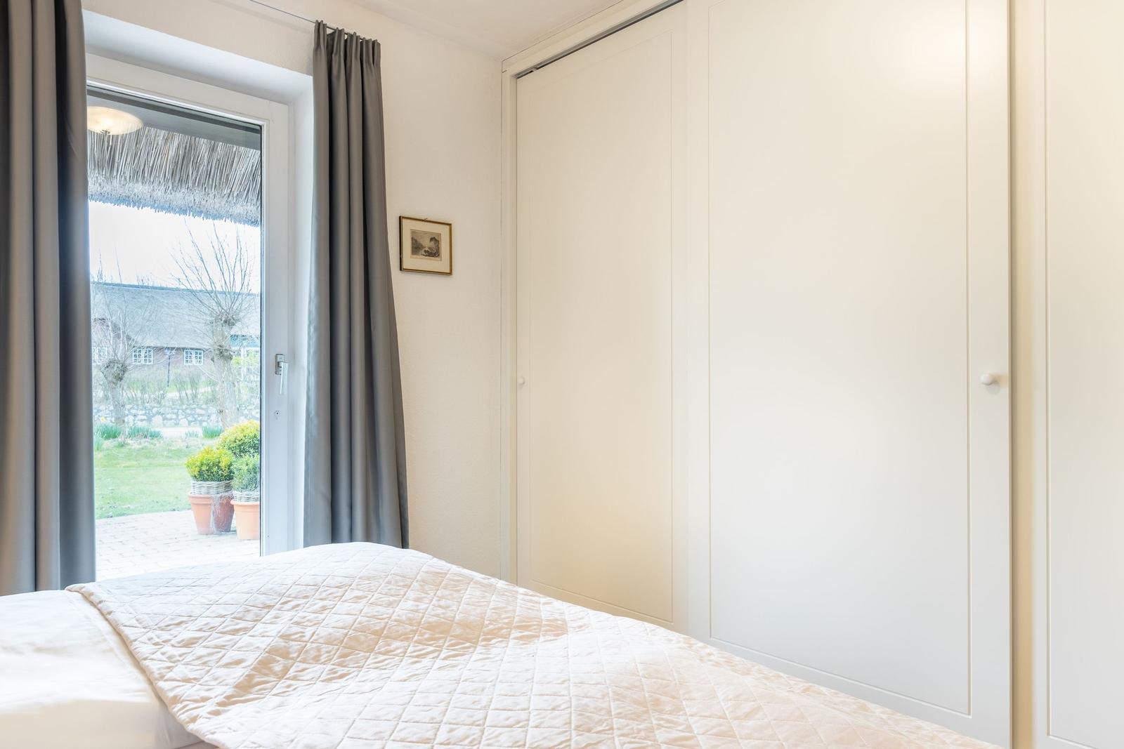 Schlafzimmer mit Bett, Kleiderschrank und Fenster zum Garten.