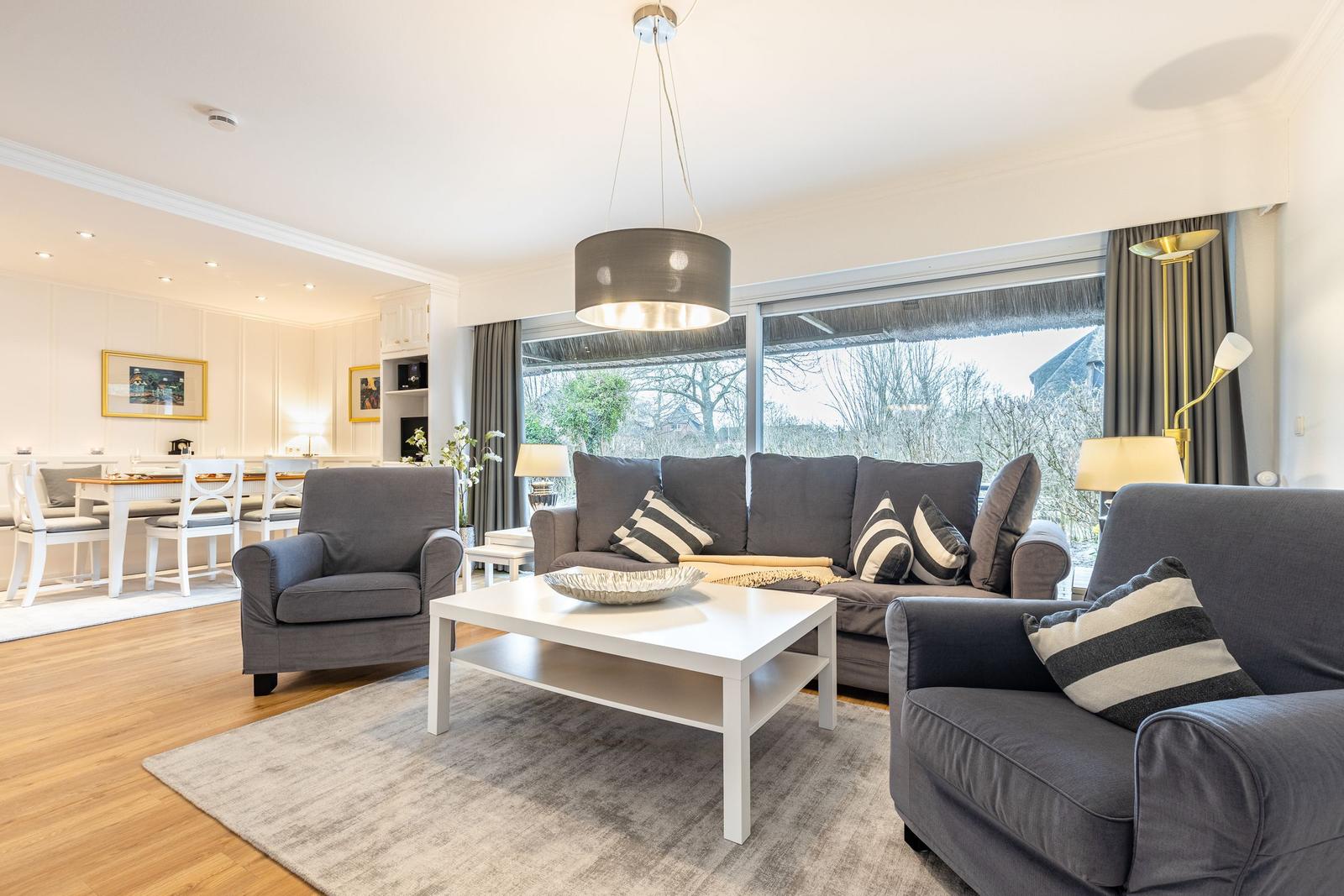 Wohnzimmer mit grauem Sofa, weißen Möbeln und großem Fenster.