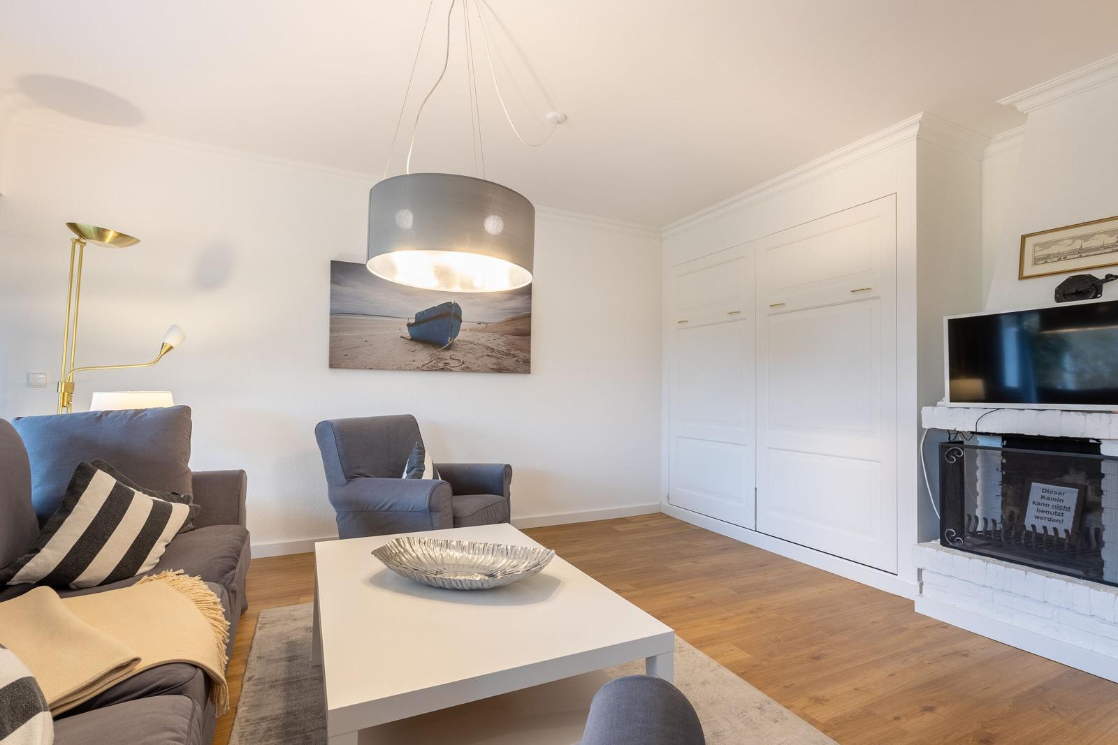 Wohnzimmer mit Sofa, Sessel, Couchtisch und Fernseher an der Wand.