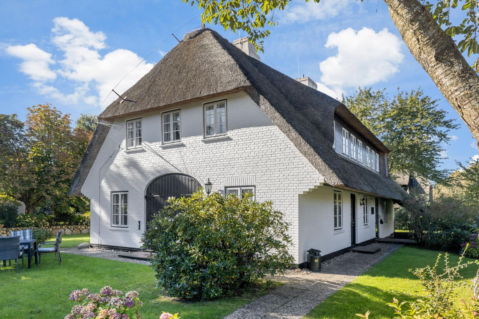 House with thatched roof, white walls, and garden. Inviting atmosphere with seating area.