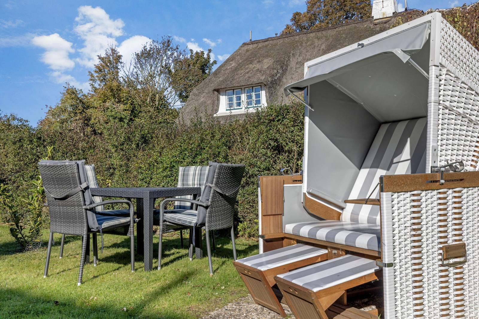 Backyard with garden furniture and beach chair. A thatched-roof house in the background.