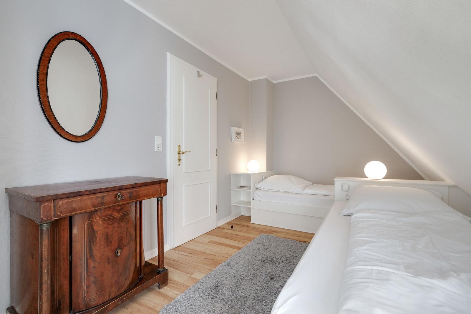 Room with two beds, wooden floor, and antique dresser under sloped ceiling.